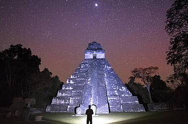 Mann erleuchtert mit Taschenlampe den Maya-Tempel Chichen Itza bei Nacht