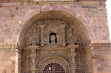 Fassade der Kirche San Lorenzo mit einem hölzernen Rundbogenportal, das von kunstvollen Steinmetzarbeiten umgeben ist und von zwei Glockentürmen flankiert wird